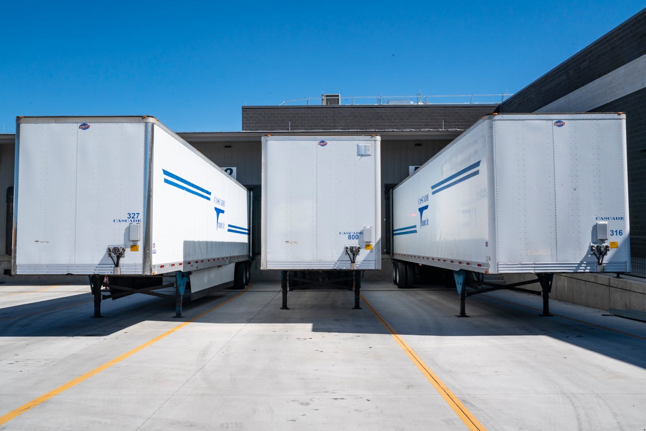 digital Three white cargo trailers parked at an industrial shipping dock under clear blue skies.